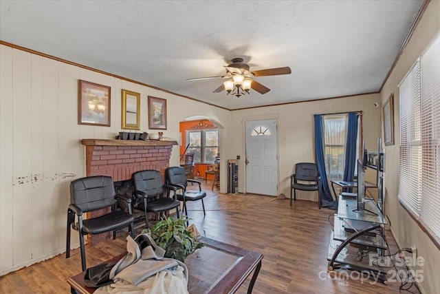 living room with crown molding, ceiling fan, hardwood / wood-style flooring, a fireplace, and a textured ceiling