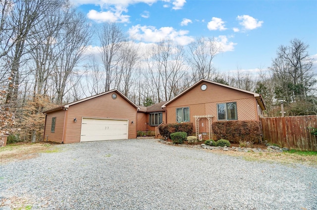 ranch-style home featuring gravel driveway, an attached garage, and fence