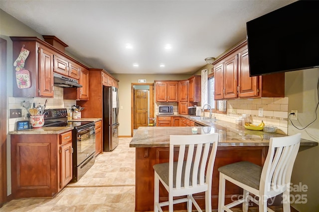 kitchen featuring stainless steel appliances, a breakfast bar area, under cabinet range hood, and a peninsula