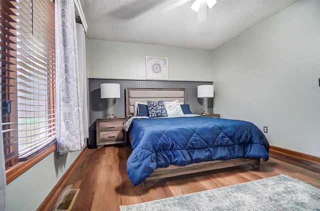 bedroom with visible vents, a ceiling fan, a textured ceiling, wood finished floors, and baseboards