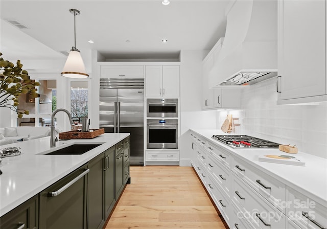 kitchen featuring sink, custom exhaust hood, white cabinetry, pendant lighting, and stainless steel appliances