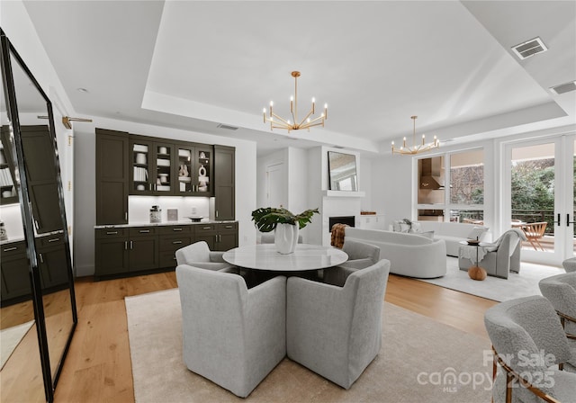 dining space with a raised ceiling, an inviting chandelier, and light hardwood / wood-style floors