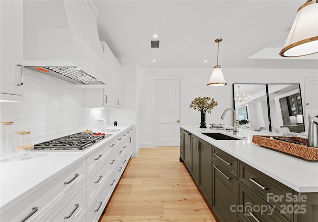 kitchen featuring white cabinetry, premium range hood, hanging light fixtures, and sink