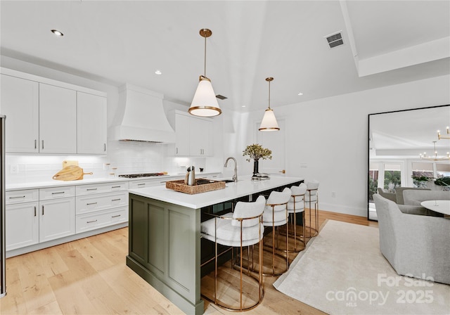 kitchen featuring white cabinetry, a kitchen island with sink, hanging light fixtures, and custom exhaust hood