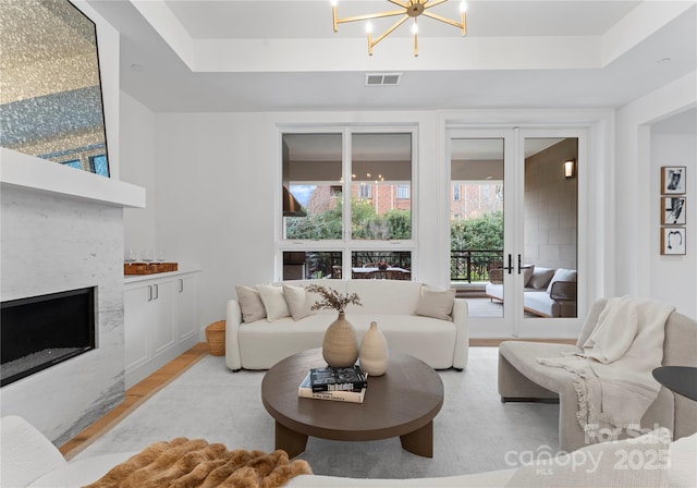 living room featuring french doors, a raised ceiling, light hardwood / wood-style floors, and a notable chandelier