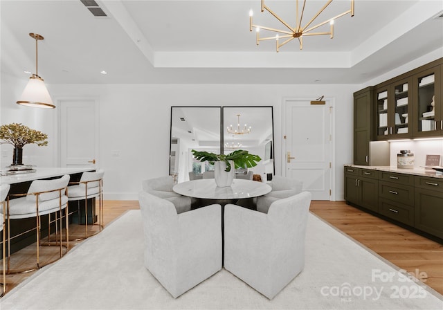 dining space featuring a tray ceiling, a chandelier, and light hardwood / wood-style floors