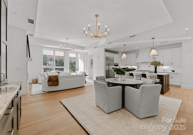 dining area with an inviting chandelier, sink, a tray ceiling, and light hardwood / wood-style floors