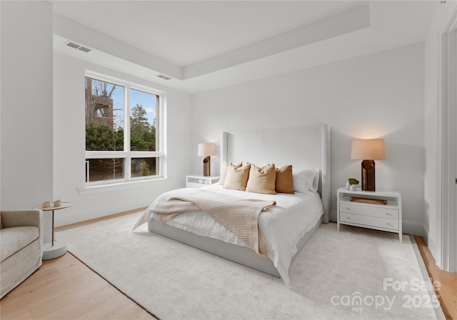 bedroom with a raised ceiling and light hardwood / wood-style flooring