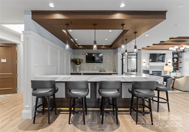 kitchen featuring a breakfast bar area, hanging light fixtures, light stone countertops, light hardwood / wood-style floors, and decorative backsplash