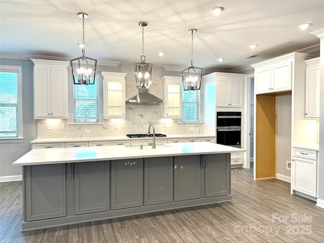 kitchen featuring a large island, wall chimney range hood, light countertops, and backsplash