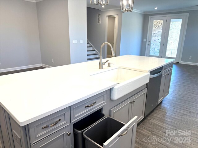 kitchen featuring wood finished floors, gray cabinets, ornamental molding, a sink, and dishwasher