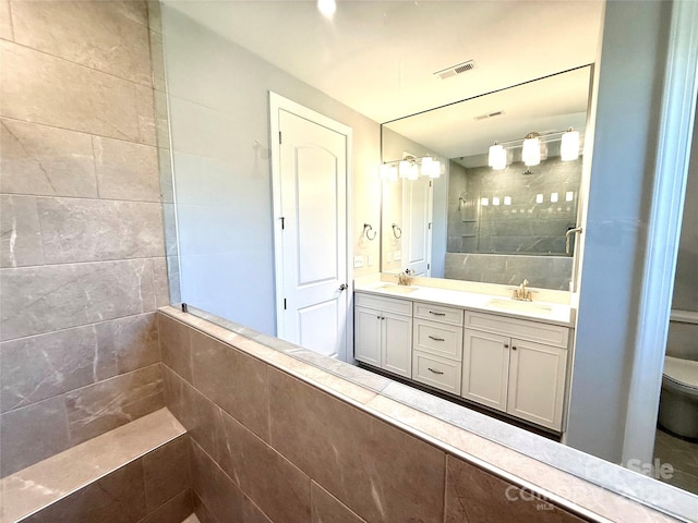 bathroom featuring double vanity, visible vents, tiled shower, and a sink