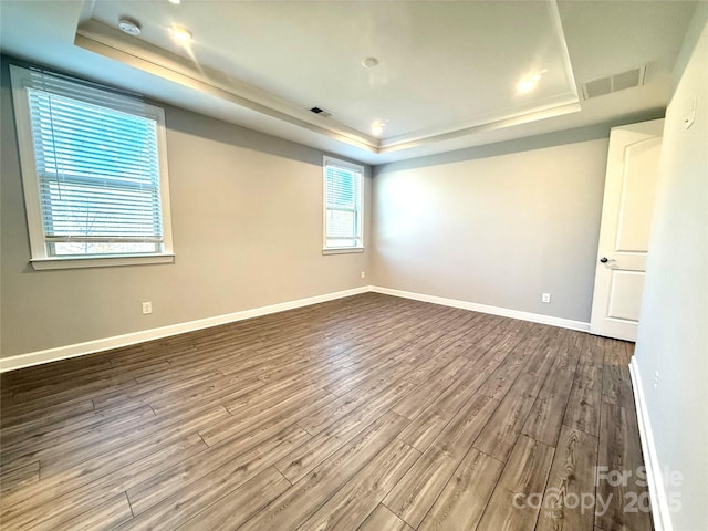 unfurnished room with a raised ceiling, wood finished floors, visible vents, and baseboards