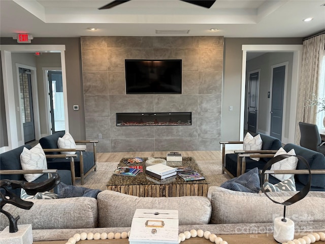 living room featuring a tiled fireplace, tile walls, and a raised ceiling