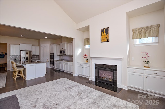 living room featuring high vaulted ceiling, sink, and dark hardwood / wood-style floors