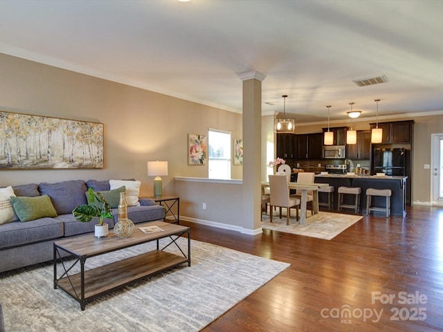 living room with crown molding, dark wood-type flooring, and decorative columns