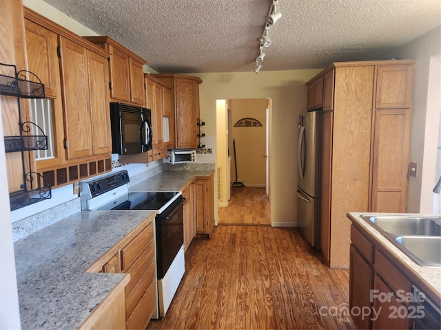 kitchen with rail lighting, sink, stainless steel refrigerator, dark hardwood / wood-style flooring, and electric stove