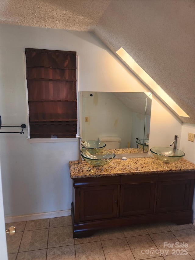 bathroom with vaulted ceiling, vanity, toilet, tile patterned floors, and a textured ceiling