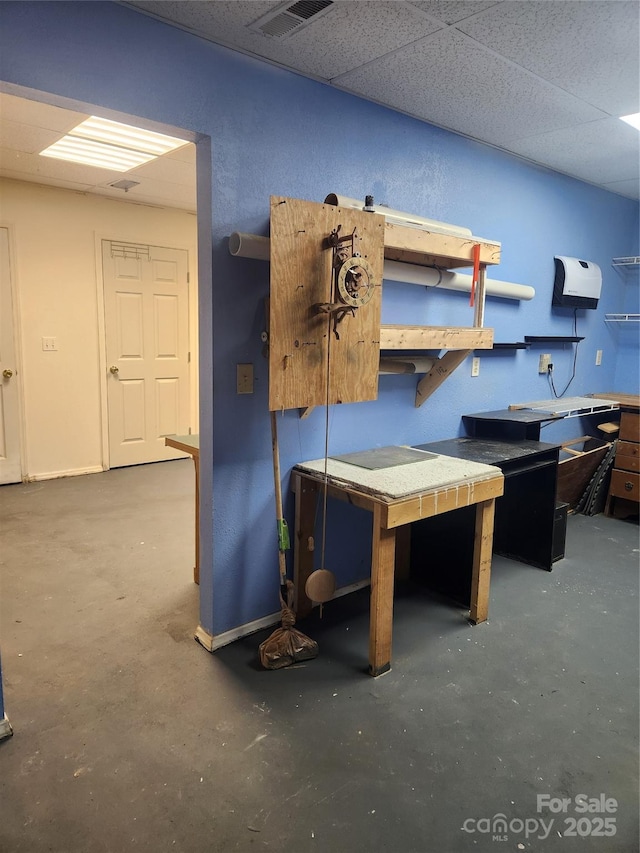 office space with a paneled ceiling, concrete flooring, and a workshop area