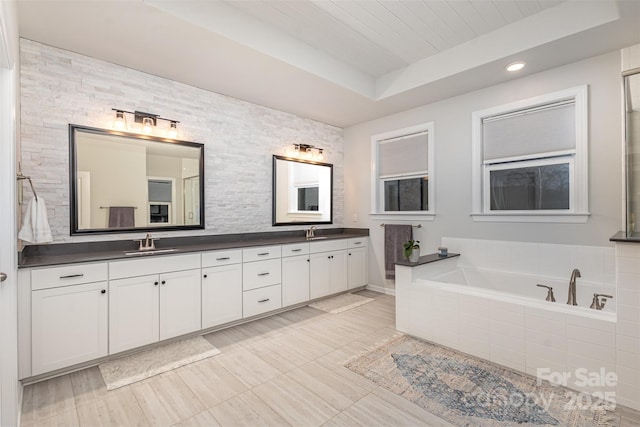 bathroom featuring tiled bath, vanity, and a raised ceiling