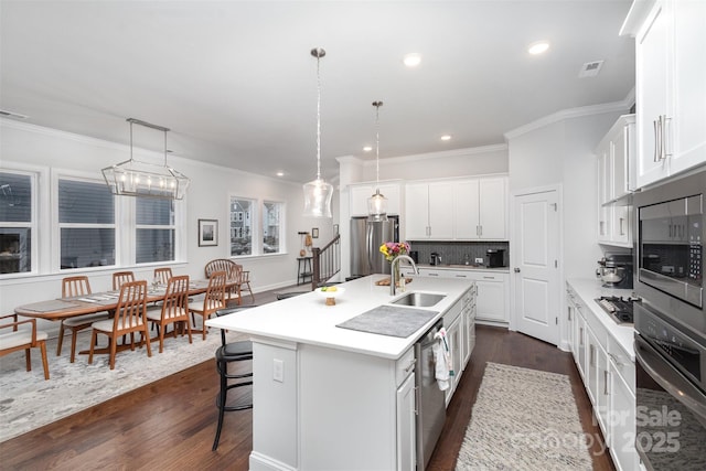 kitchen featuring decorative light fixtures, sink, a kitchen island with sink, stainless steel appliances, and white cabinets