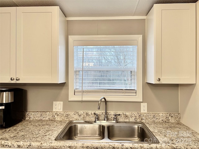 kitchen featuring light stone countertops, sink, white cabinetry, and a textured ceiling