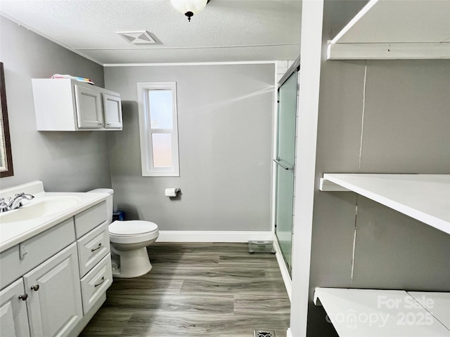 bathroom with a textured ceiling, an enclosed shower, vanity, toilet, and hardwood / wood-style flooring