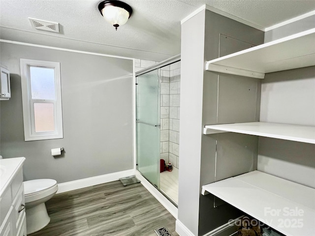 bathroom featuring toilet, vanity, hardwood / wood-style flooring, a textured ceiling, and an enclosed shower