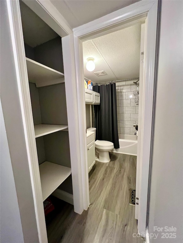 full bathroom featuring a textured ceiling, vanity, shower / tub combo, toilet, and hardwood / wood-style flooring