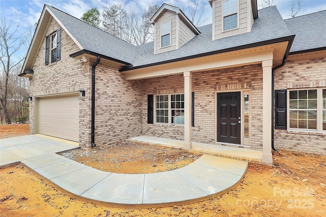 cape cod home with a shingled roof, a porch, concrete driveway, and brick siding