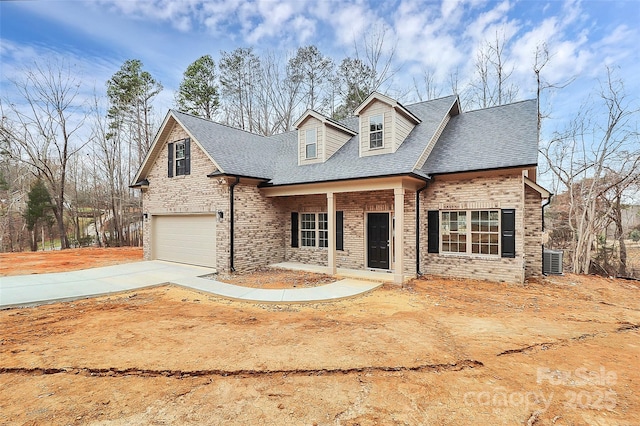 new england style home with an attached garage, a shingled roof, concrete driveway, and brick siding