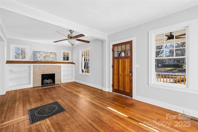 unfurnished living room featuring hardwood / wood-style floors, built in features, a fireplace, and plenty of natural light