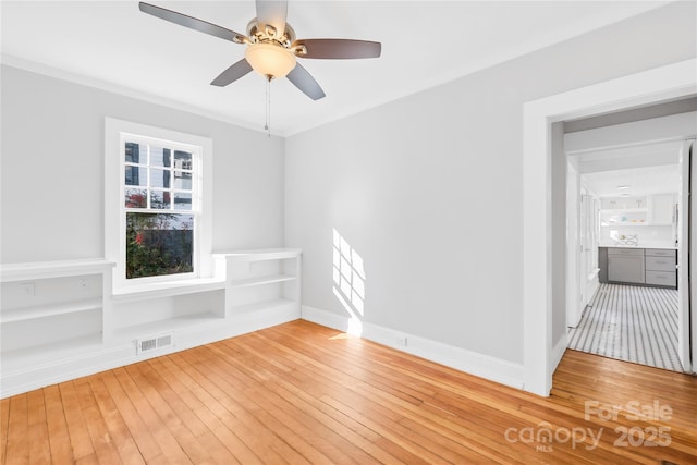 empty room with ceiling fan, crown molding, built in features, and hardwood / wood-style flooring