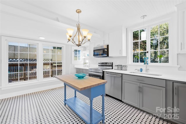 kitchen featuring appliances with stainless steel finishes, decorative light fixtures, a chandelier, white cabinets, and sink