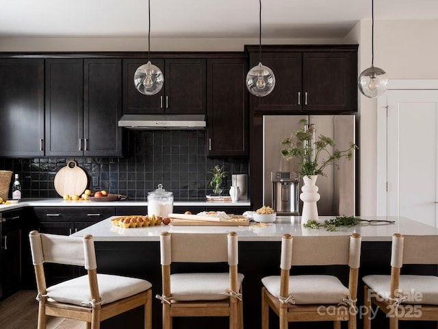 kitchen with tasteful backsplash, a breakfast bar area, hanging light fixtures, hardwood / wood-style flooring, and stainless steel fridge with ice dispenser