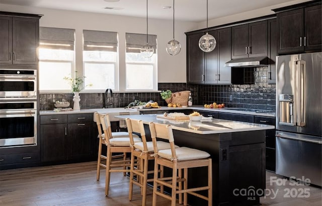 kitchen featuring pendant lighting, a breakfast bar, appliances with stainless steel finishes, a center island, and decorative backsplash