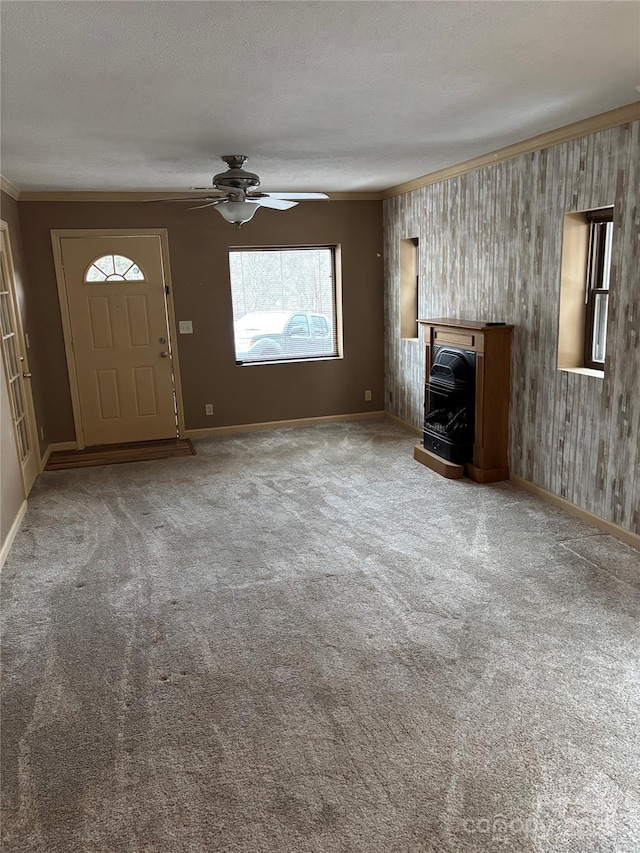 unfurnished living room with ceiling fan, wood walls, crown molding, carpet flooring, and a textured ceiling