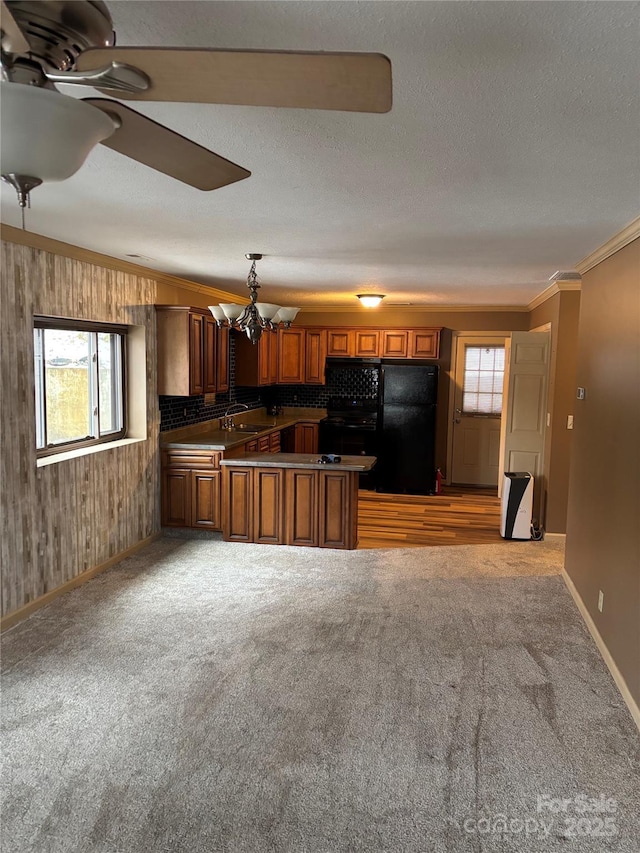 kitchen with kitchen peninsula, black fridge, hanging light fixtures, ornamental molding, and sink