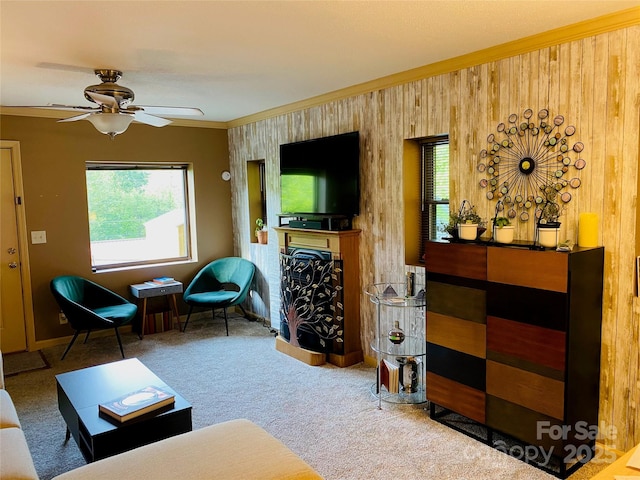 carpeted living room with ceiling fan, ornamental molding, and wooden walls