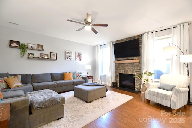 living room with ceiling fan, a stone fireplace, and hardwood / wood-style floors