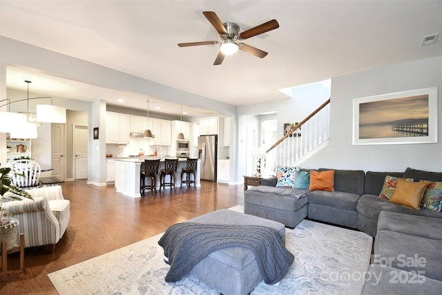 living room featuring ceiling fan with notable chandelier and dark wood-type flooring