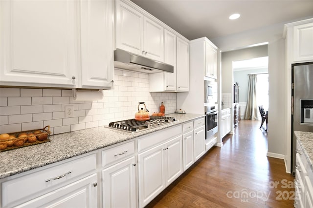 kitchen featuring appliances with stainless steel finishes, white cabinetry, backsplash, light stone countertops, and dark wood-type flooring