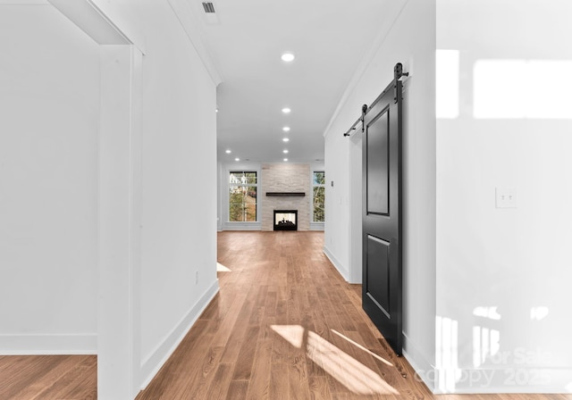 corridor with ornamental molding, a barn door, and wood-type flooring