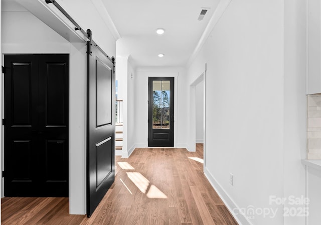 foyer entrance with a barn door, crown molding, and hardwood / wood-style floors