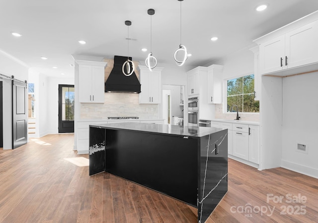 kitchen featuring premium range hood, a barn door, white cabinets, and a center island