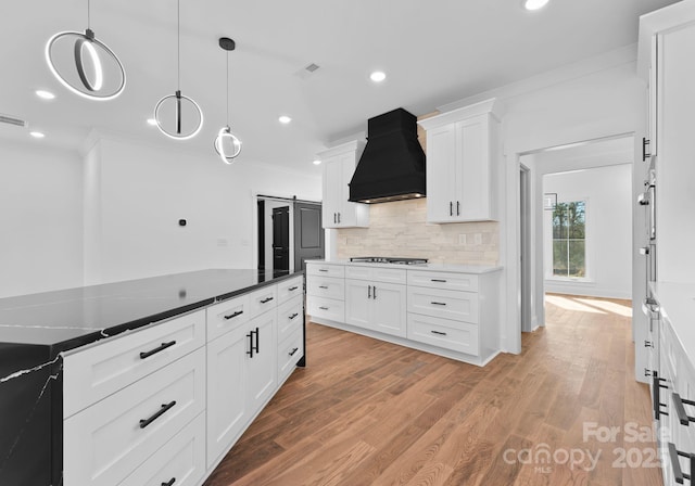 kitchen with premium range hood, a barn door, light hardwood / wood-style floors, pendant lighting, and white cabinets