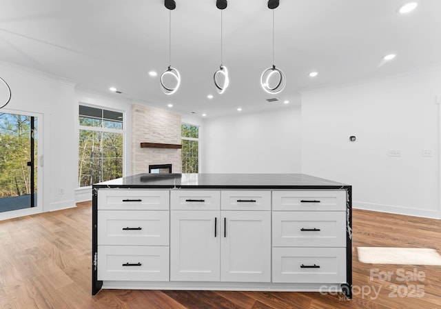 kitchen with decorative light fixtures, white cabinetry, a fireplace, light hardwood / wood-style flooring, and crown molding