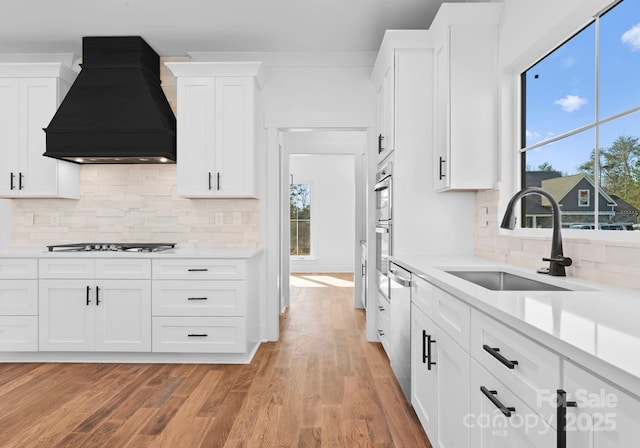 kitchen featuring white cabinetry, appliances with stainless steel finishes, light wood-type flooring, custom range hood, and sink