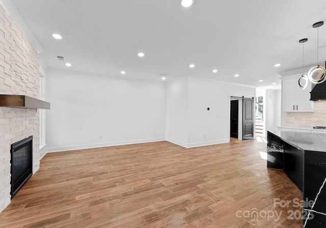 unfurnished living room with crown molding, a barn door, light wood-type flooring, and a stone fireplace