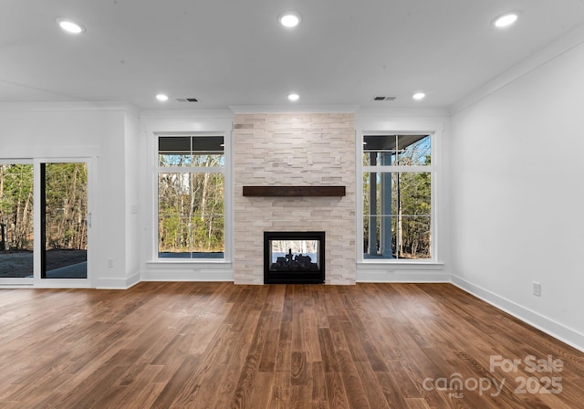 unfurnished living room with hardwood / wood-style flooring, ornamental molding, and a stone fireplace